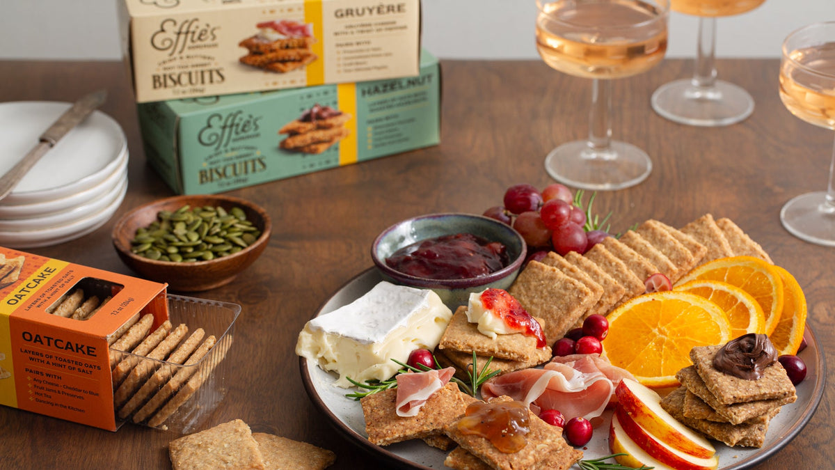 Board of Effie's Oatcake biscuits with brie, prosciutto, jam, cranberries and orange slices, with Gruyère and Hazelnut boxes behind.